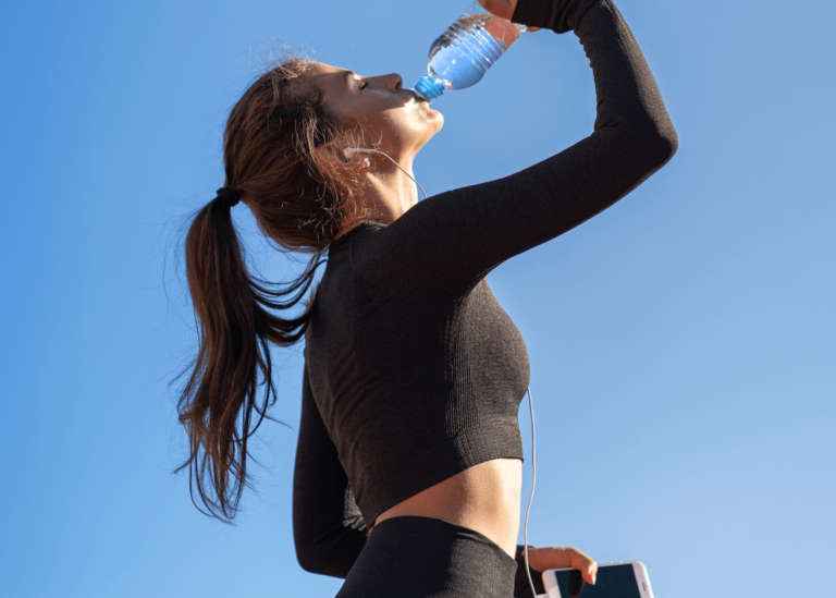 Athletic women drinking from water bottle with blue sky